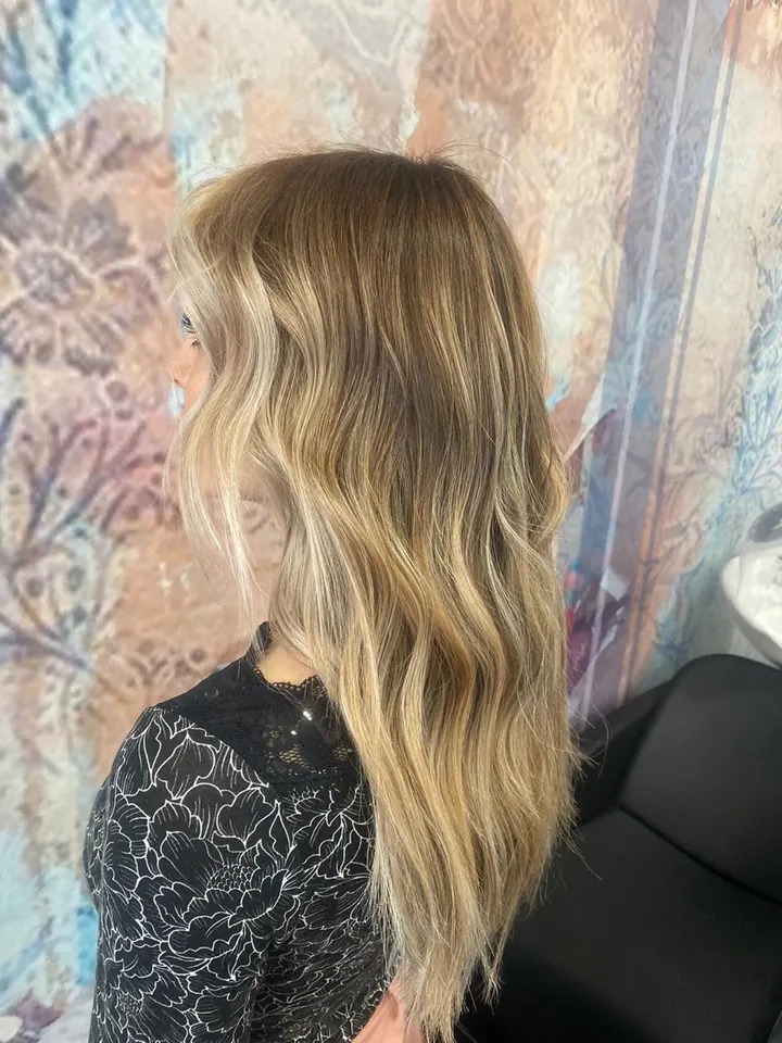 Capelli lunghi biondi con la radice più scura, di profilo, davanti alla carta da parati del salone