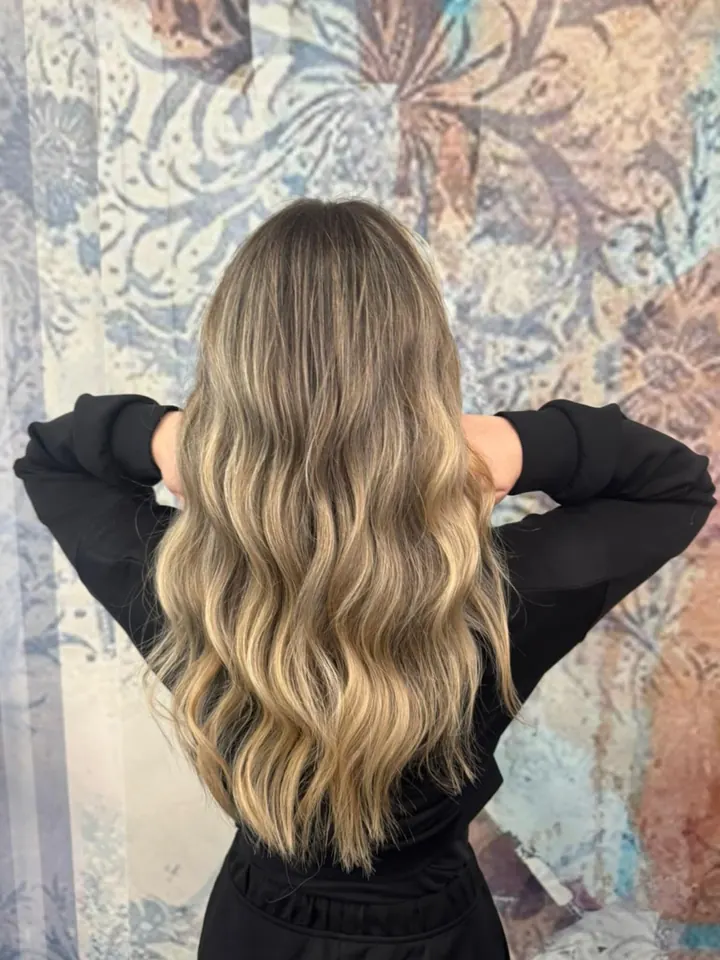 Capelli lunghi mossi, dal castano al biondo, di spalle davanti alla parete col volto di donna