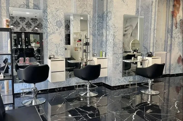 Le postazioni del salone: poltrone nere, specchi e carta da parati a fiori azzurri